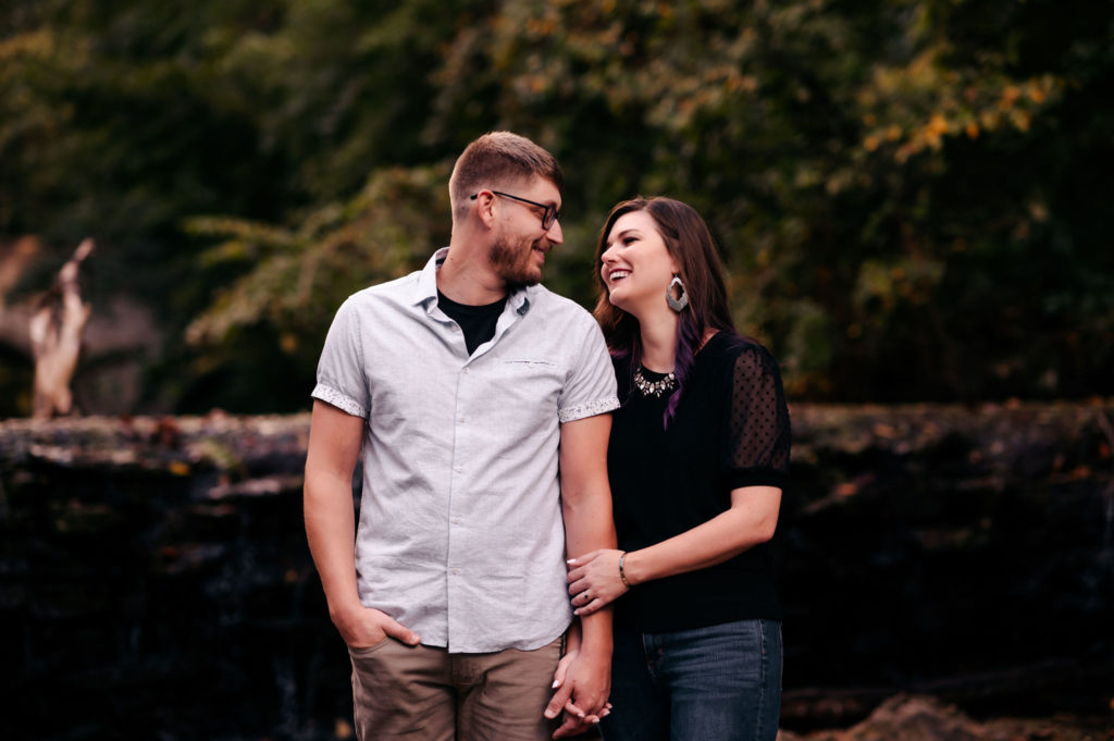 a couple laughs together while standing outdoors for their engagement photo session. 