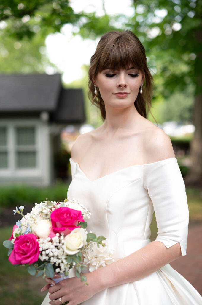 A bride stands in her elegant gown while holding her bouquet of white and pink flowers. 