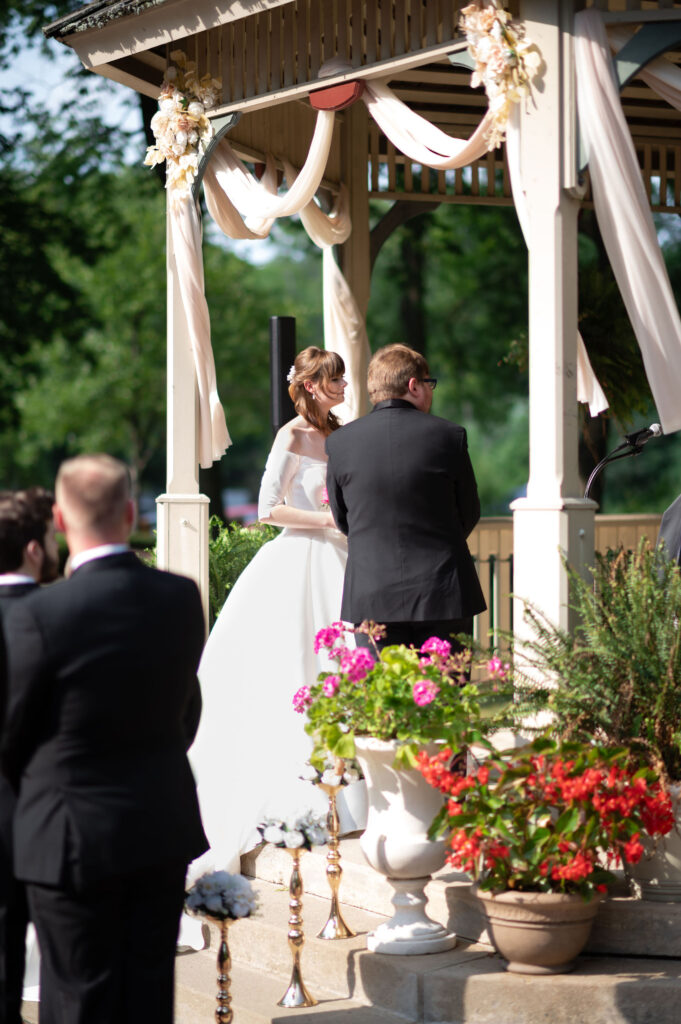 A bride and groom look towards the officiant during the ceremony while being lit up by the warm glow of the sun. 