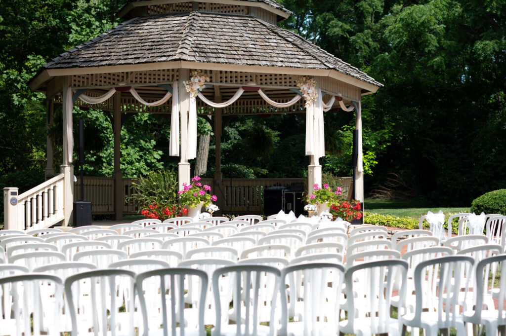 An empty ceremony space shows the setup before any guests arrive. White chairs lined up neatly before a brightly lit gazebo at Benham's Grove wedding venue. 