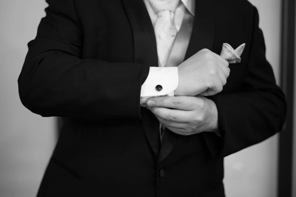 A black and white image showing the details of a groom getting ready for his wedding day, featuring him getting on his cufflinks. 